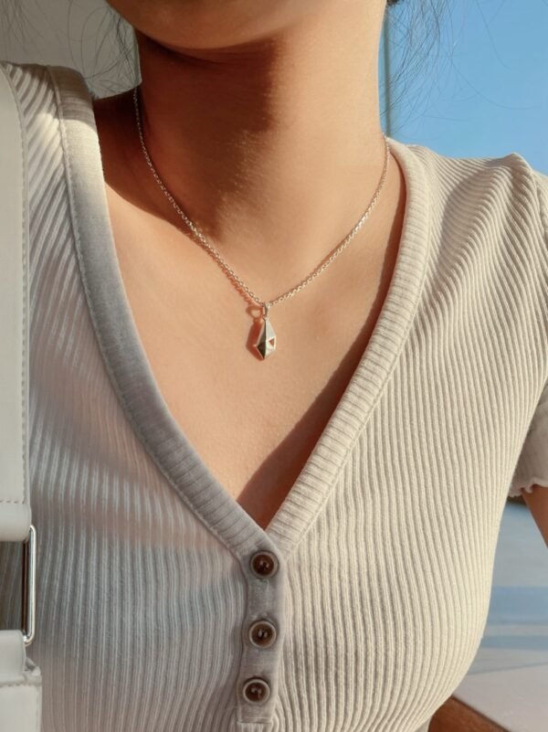A silver geometric pendant necklace on model's neck, minimalist modern design